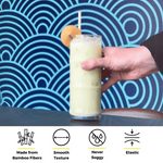 Hand holding a tall green smoothie with a bamboo fiber straw and a cookie garnish, set against a bold blue wave pattern background with icons showcasing the straw’s features—never soggy, elastic, and smooth texture.