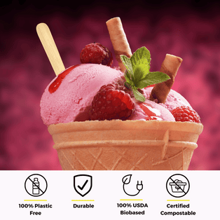 A waffle cone filled with strawberry ice cream topped with fresh raspberries, a sprig of mint, and a rolled wafer, with an unwrapped bamboo dessert spoon from Holy City Straw Co. inserted into the scoop. Below the cone are icons with text stating 