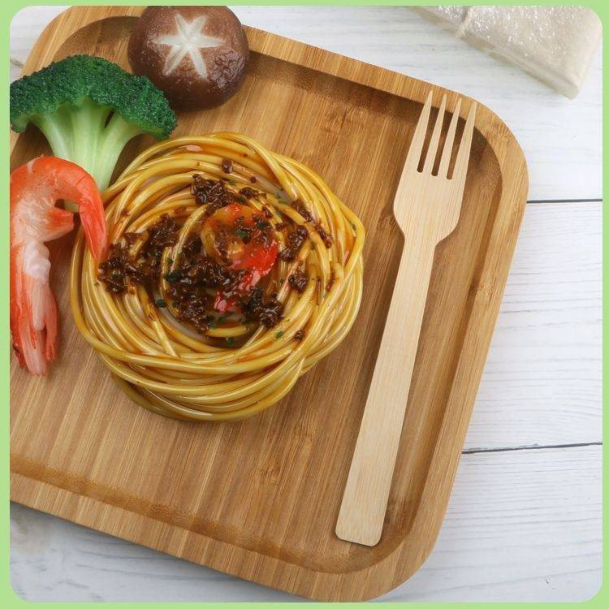 Wooden tray with pasta, broccoli, shrimp, and a mushroom, accompanied by a Holy City Straw Co. bamboo fork.