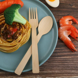 A Holy City Straw Co. bamboo knife and fork set elegantly placed on a teal plate with spaghetti in tomato sauce, garnished with a vibrant broccoli floret. To the side, there's a perfectly cooked shrimp and a half-sliced boiled egg, showcasing a variety of textures and colors on a rustic wooden tabletop.