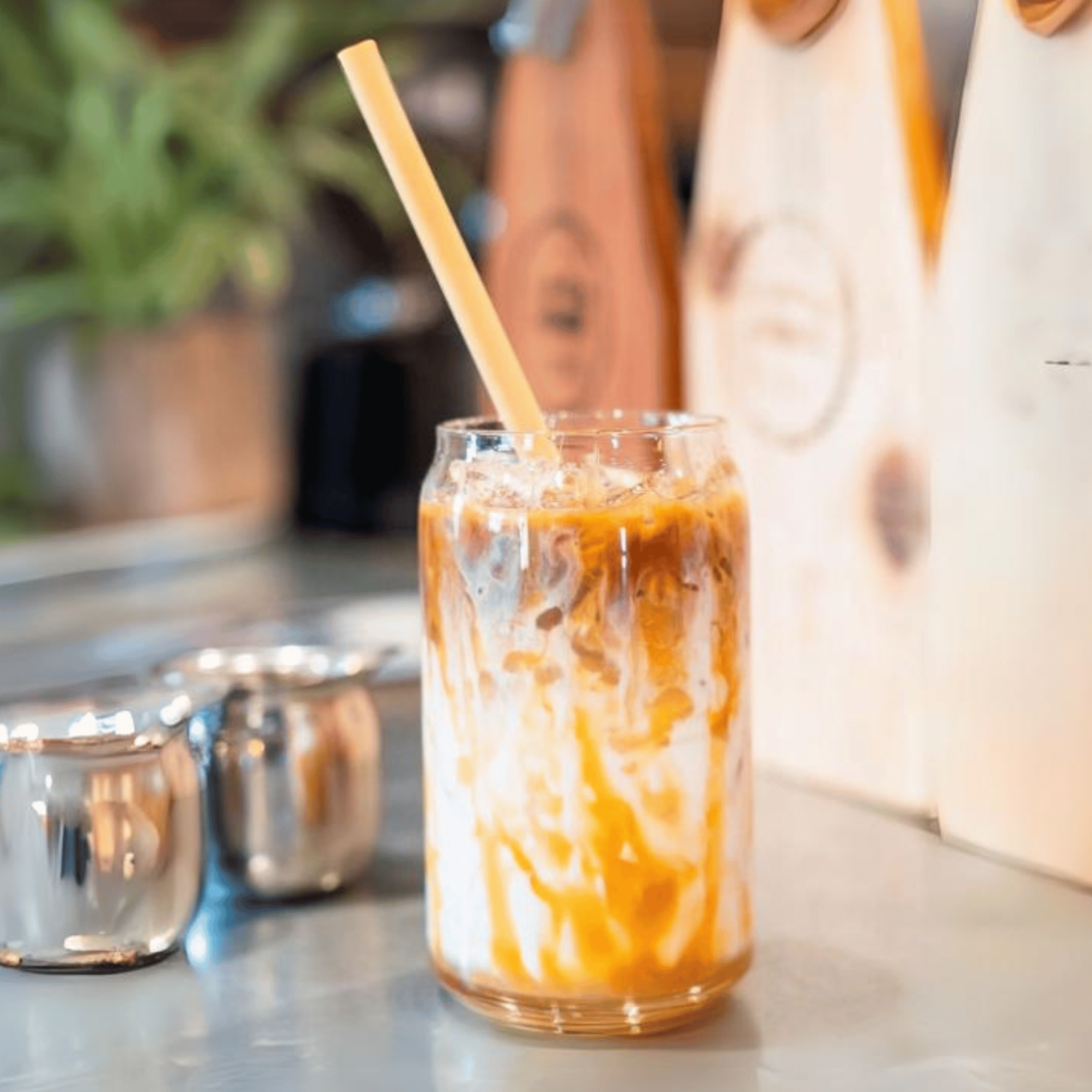 Glass of iced caramel macchiato with a Holy City Straw Co. giant reed stem straw, on a café counter.