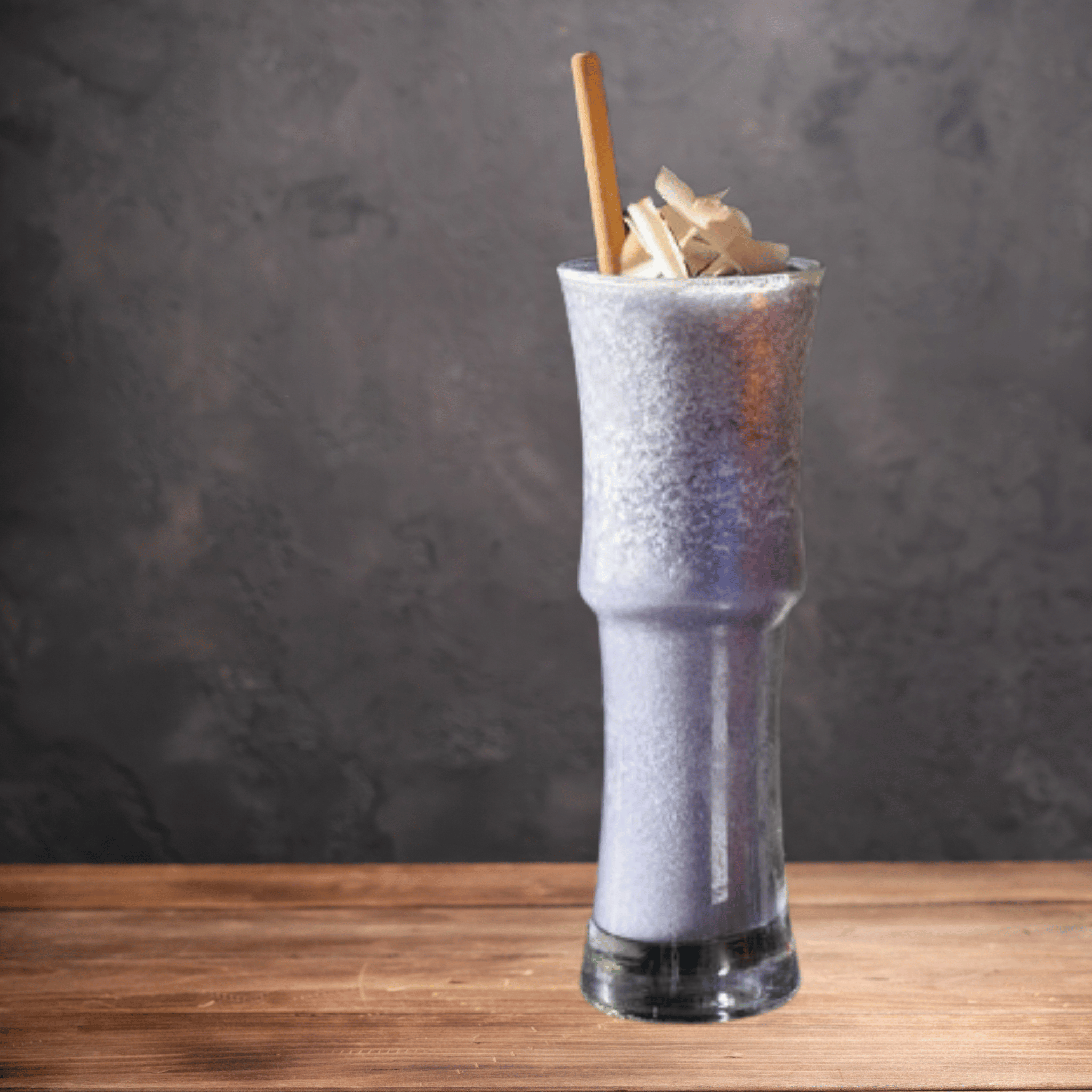 Tall glass with a purple smoothie, topped with shavings and a Holy City Straw Co. giant reed stem straw, against a dark background