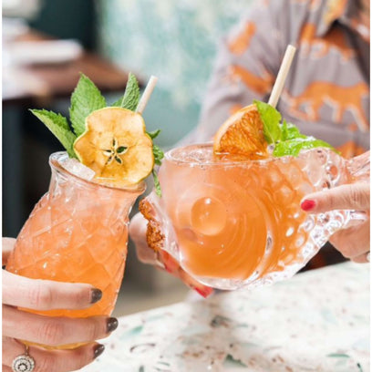 Two hands cheersing island cocktail with wheat straw