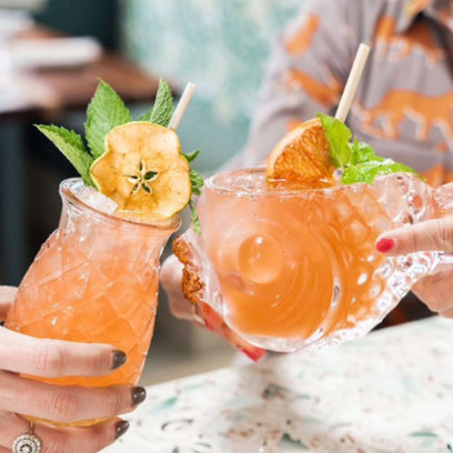 two hands cheersing island cocktail with wheat straw